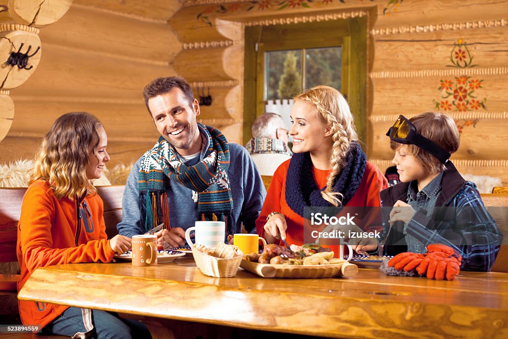 Happy family having lunch in restaurant after skiing Mother, father and their children wearing winter clothes sitting in a mountain restaurant after skiing, talking and enjoying dinner. Apres-Ski Stock Photo