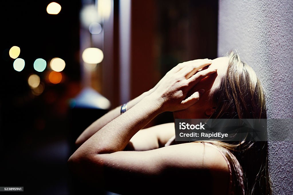 Despairing blonde, hands over face, in nighttime street scene A blonde woman with her hands over her face seems very upset as she stands outside in a nighttime street. Copy space on the bokeh street lights. Head In Hands Stock Photo