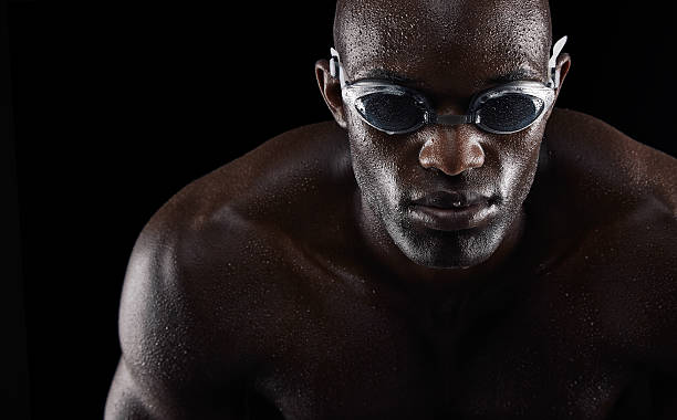 Young african swimmer Portrait of a young african man wearing swimming goggles isolated on black background. Fit young athlete. professional sportsperson stock pictures, royalty-free photos & images