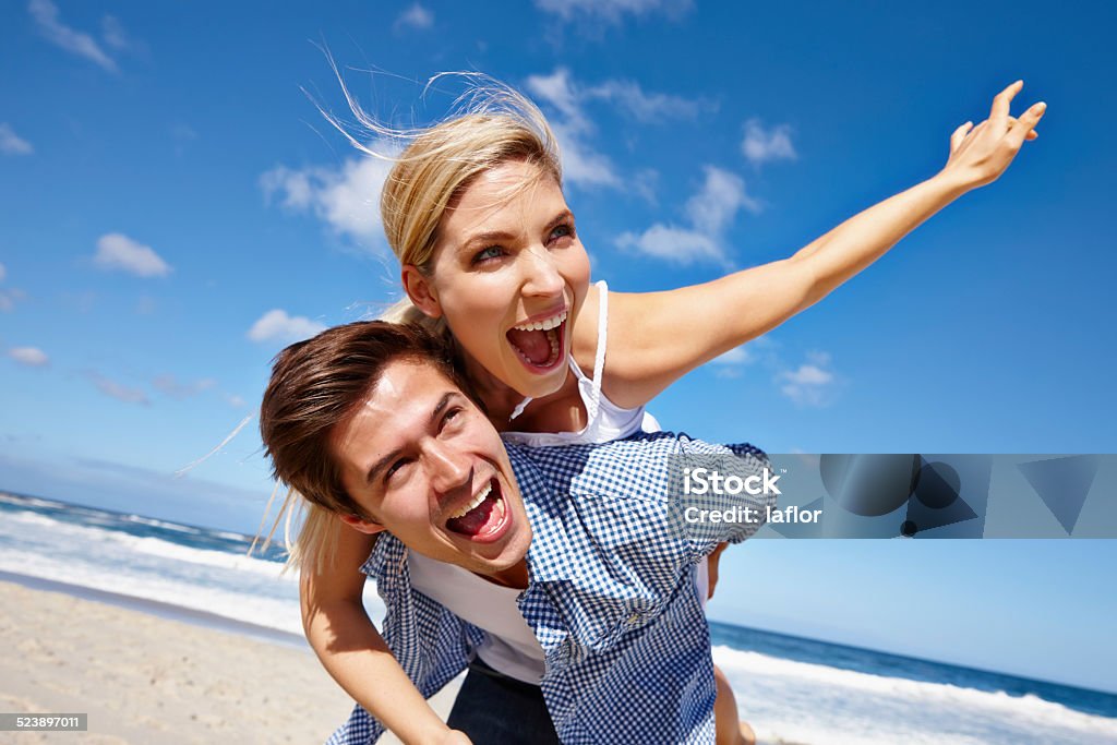 It's summer, baby! Shot of a young man giving his girlfriend a piggyback ride at the beach Adult Stock Photo
