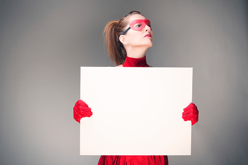 A woman with a serious expression dressed in a superher costume holding a blank sign.