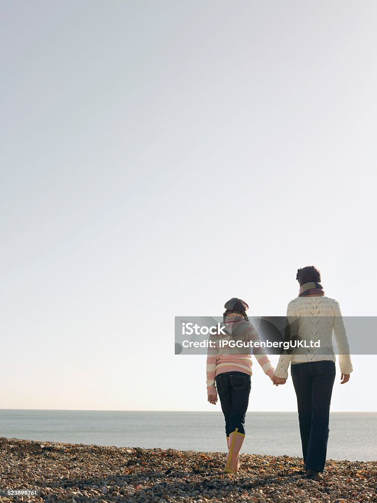 Mother And daughter Holding Hands Full length rear view of mother and daughter holding hands and walking on beach Adult Stock Photo