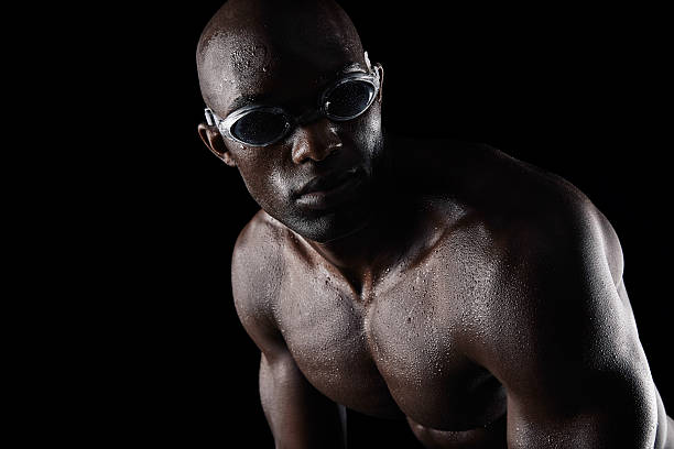 African male athlete with swimming goggles looking away on black background. Professional swimmer practicing.