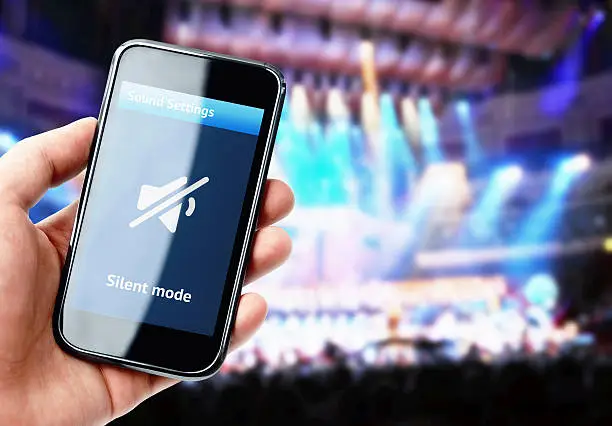 Photo of Hand holding smartphone with mute sound during concert