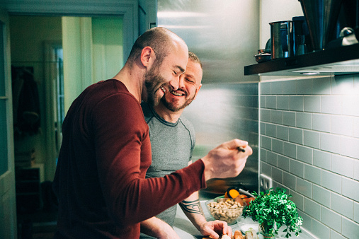 homosexual couple stands together in the kitchen at the stove and tasting the meal