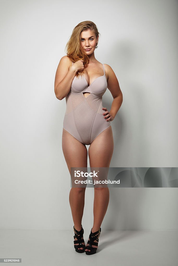 Beautiful plus-size woman in sexy lingerie Full length image of beautiful plus-size woman in sexy lingerie and stilettos over grey background. Voluptuous woman posing proudly in body stocking. Women Stock Photo