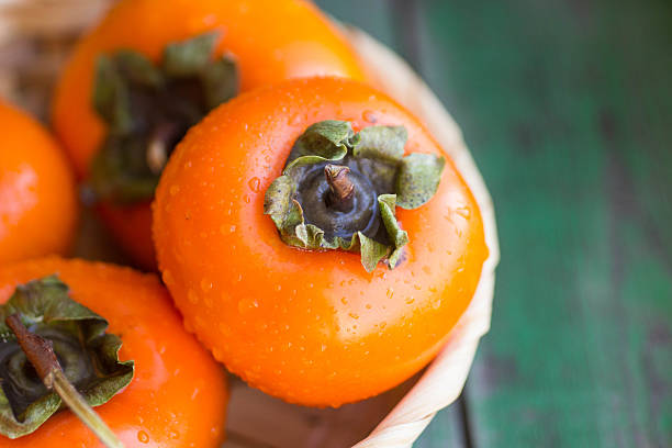 спелые persimmons in a wicker basket - persimmon стоковые фото и изображения