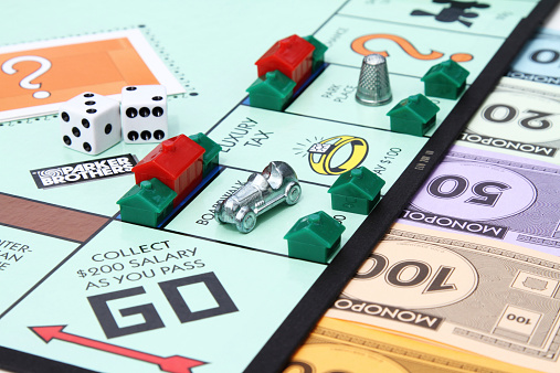 West Palm Beach, USA - August 16, 2013: A partial view of a Monopoly game board showing the Go start square with various game playing pieces set up on the board.  Game pieces visible include dice, hotel and house property pieces, game currency and the Race Car and Thimble game tokens.  Monopoly is a popular board game that is owned and distributed by Hasbro.