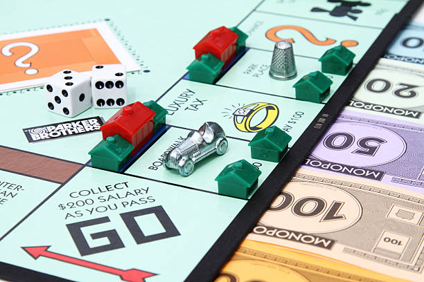 Monopoly game Go square West Palm Beach, USA - August 16, 2013: A partial view of a Monopoly game board showing the Go start square with various game playing pieces set up on the board. Game pieces visible include dice, hotel and house property pieces, game currency and the Race Car and Thimble game tokens. Monopoly is a popular board game that is owned and distributed by Hasbro. board game piece stock pictures, royalty-free photos & images