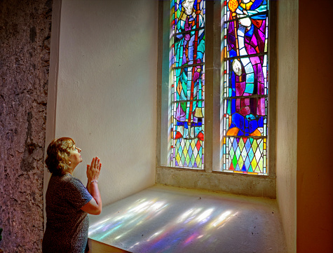 Mature hispanic woman praying at church window