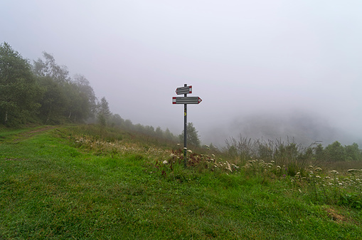 Pointer to a hiking trail in the mountains covered with dense fog. Italian Alps.