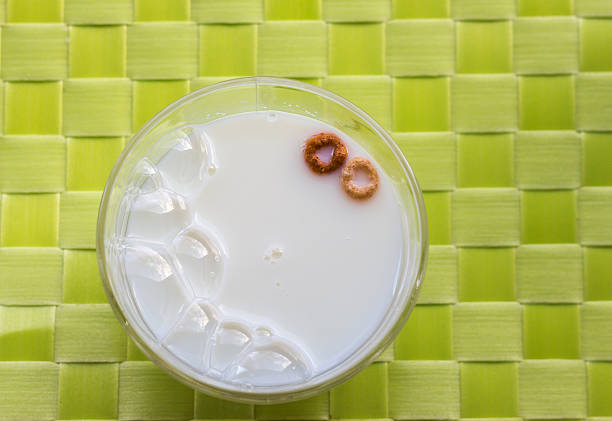 horizontal image of a glass bowl of milk with bubbles and two cheerios floating in the milk on lime green weave pattern background.