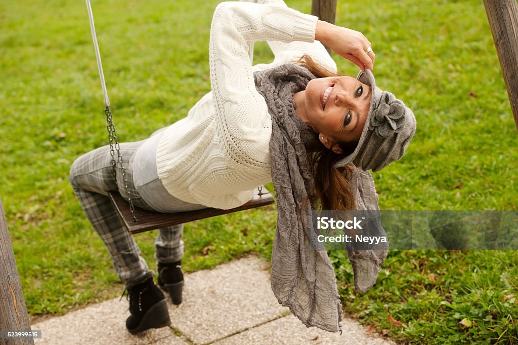 Beautiful Woman on a Swing Attractive woman in autumn fashioned clothings sitting on a swing and looking backward and smiling. Horizontal color image. Green grass copy space. Mature Adult Stock Photo