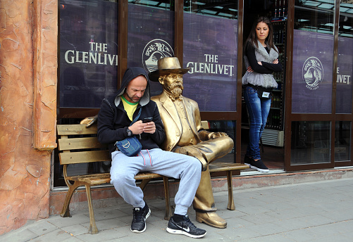 Veliko Tarnovo, Bulgaria - March 19, 2016: Unidentified Caucasian man and girl next to the golden sitting statue of an unidentified gentleman in the center of the town