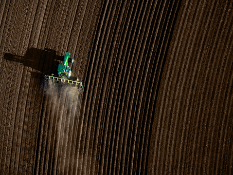 Lubbock, Texas, USA - March 15, 2016: A  John Deere  tractor is plowing a barren field for future crops. As the tractor moves, dust and dirt can be seen behind the tractor. Vertical lines radiate from either side of the tractors. The tractor's shadow can be seen. Photo shot from high angle viewpoint.