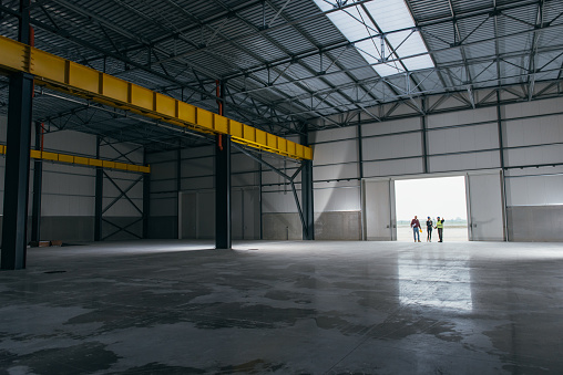 Architect team At Work Site With Blueprints standing at big hangar doors