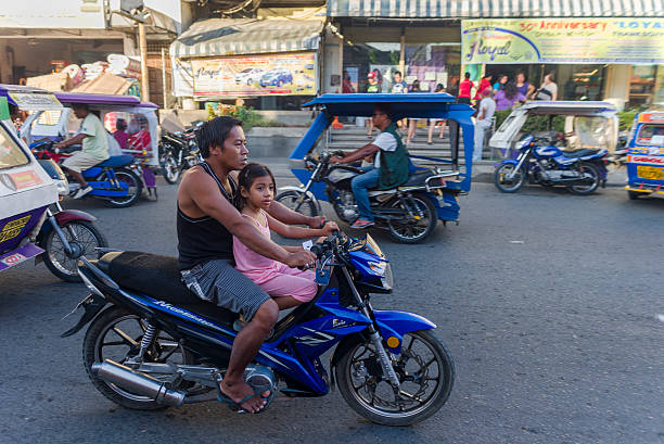 Transport in Philippines. Iloilo, Philippines - February 13, 2016. Motorcycle transport in Iloilo Philippines. Father and daughter on the motorcycle and there are some tricycle on the road. philippines tricycle stock pictures, royalty-free photos & images