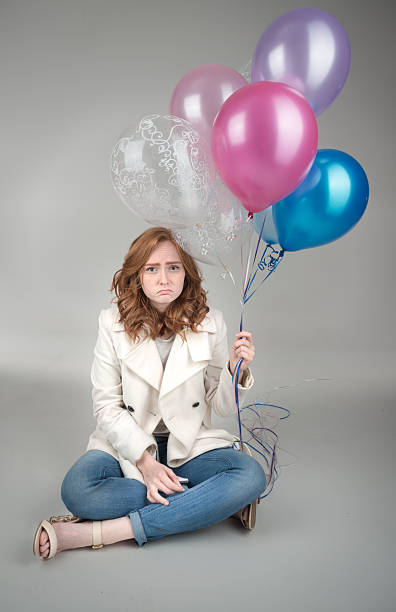 istock Sad young adult sitting on floor holding balloons 524019092