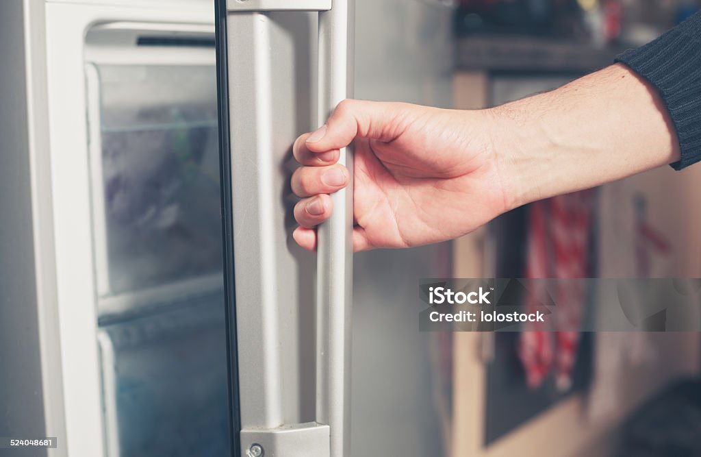 Hand opening freezer door The hand of a young man is opening a freezer door Freezer Stock Photo