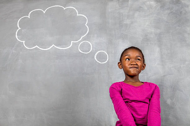 fille africaine penser dur assis en face de tableau - blackboard child thinking little girls photos et images de collection