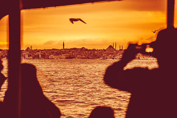 Istanbul cityscape at dusk seen from a boat on Bosphorus, blurred tourists taking pictures on foreground.