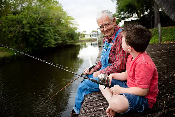 Color image of a happy senior grandfather sitting on a dock while fishing with his young great grandson.