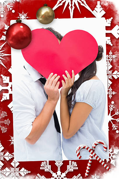 Couple covering their kiss with a heart Couple covering their kiss with a heart against christmas themed page person holding frame over face stock pictures, royalty-free photos & images
