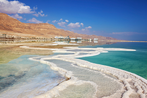 Israeli coast of the Dead Sea. Path from the salt winds picturesquely in salt water. Hotels on the bank are reflected in smooth water