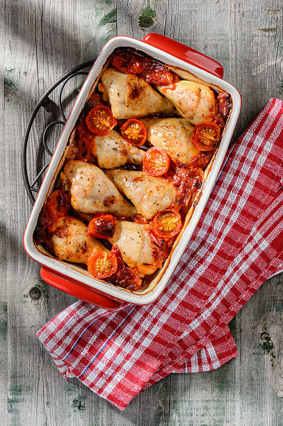 Baked chicken drumsticks in sauce with tomatoes, onion and garlic stock photo