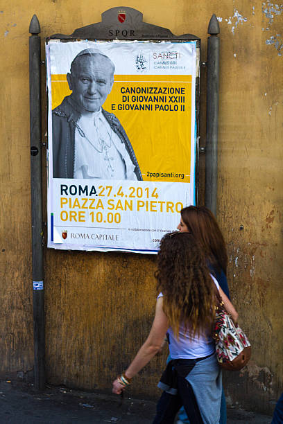 Poster Announcing Canonization of Popes Rome, Italy - April 14, 2014: Two women walk by a poster in Rome, Italy announcing the upcoming canonization  (taking place on April 27, 2014) of Pope John XXII and Pope John Paul II.  pope john paul ii stock pictures, royalty-free photos & images