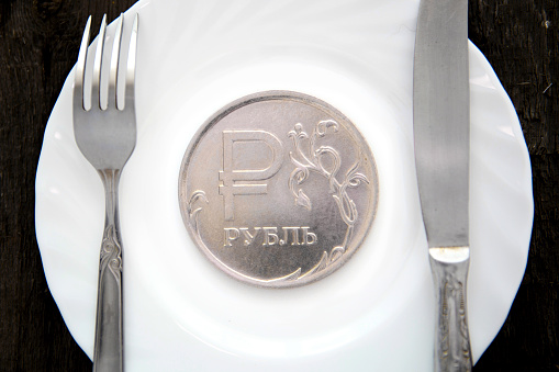 One ruble coin on a white plate next to fork and knife