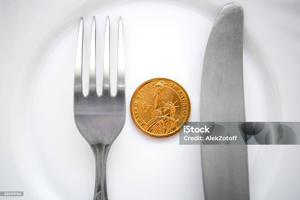 One dollar coin on a white plate One dollar coin on a white plate next to fork and knife Blank Stock Photo