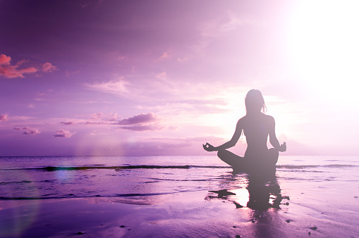 Silhouette of woman in lotus position sitting in sea and meditating