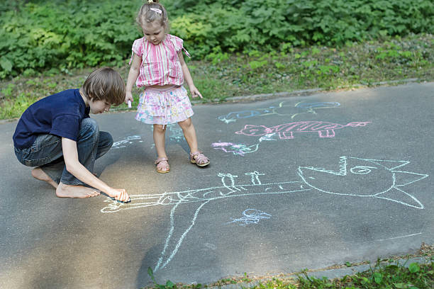 Hermanos los niños comparten la acera tizas y dibujo sobre superficies de asfalto - foto de stock