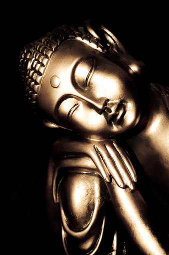 Relaxed golden buddha statue with a black background                  