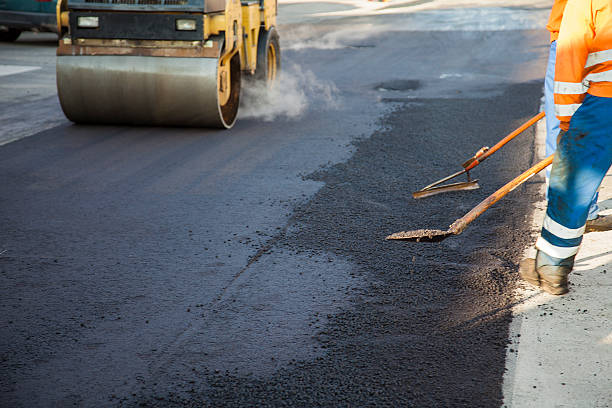 Laying new layer of asphalt Two manual workers helping to level the asphalt surface for a steamroller to press. asphalt stock pictures, royalty-free photos & images
