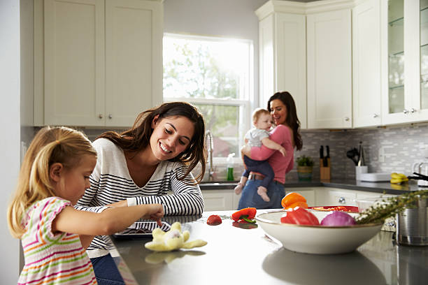 chica usa tableta en cocina con mamá y bebé madre sosteniendo otra - standing digital tablet couple love fotografías e imágenes de stock