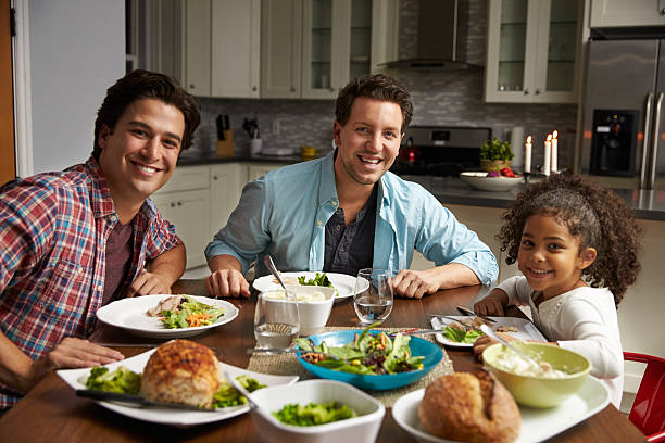 Male couple and black daughter dining at home look Male couple and black daughter dining at home look to camera gay dinner table stock pictures, royalty-free photos & images