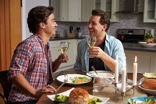 Male gay couple making a toast at dinner in their Male gay couple making a toast at dinner in their kitchen gay dinner table stock pictures, royalty-free photos & images