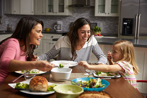 Female gay couple and daughter having dinner in their kitchen Female gay couple and daughter having dinner in their kitchen gay long hair stock pictures, royalty-free photos & images