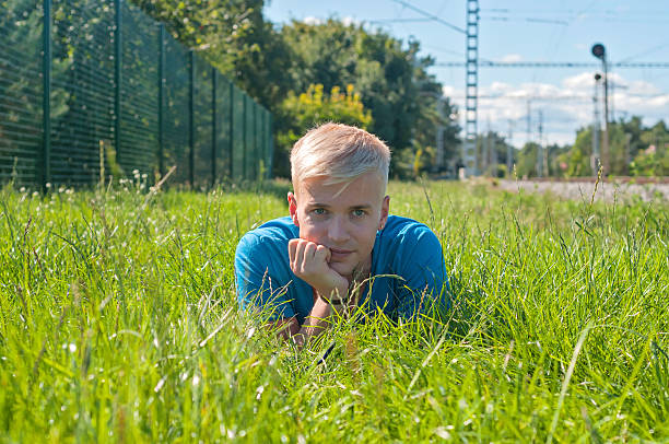 Young guy an in blue t-shirt lying on the grass and watching on you