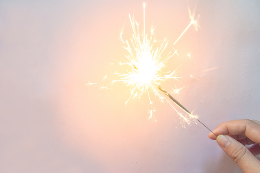 man's hand holding a sparkler on the  pink background