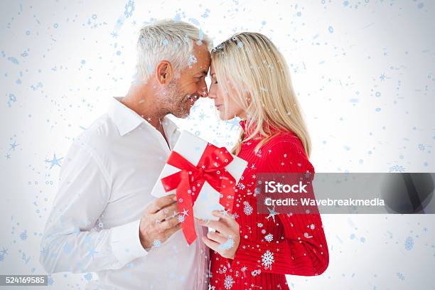 Smiling Couple Passing A Wrapped Gift Stock Photo - Download Image Now - 30-39 Years, 35-39 Years, 50-54 Years