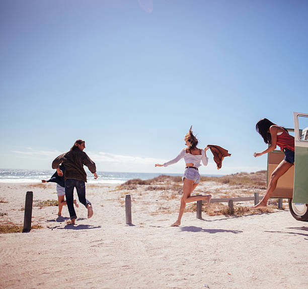 Hipster friends jumping out of Road Trip van at beach Multi-Ethnic group of road trip friends jumping out of retro van barefoot and running at sunny sandy beach hopper car stock pictures, royalty-free photos & images