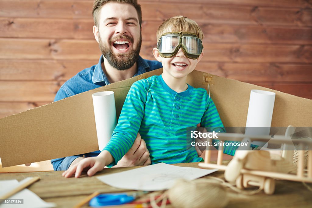 Family of pilots Cute boy with carton airplane behind back and his father looking at camera and laughing Craft Stock Photo