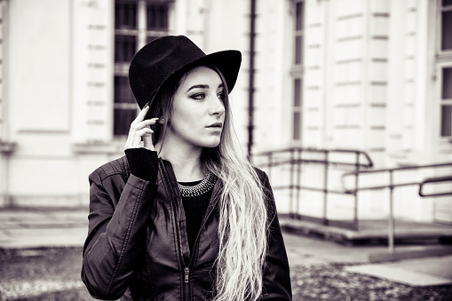 Portrait of attractive blonde young woman in black fedora hat and leather jacket looking at camera