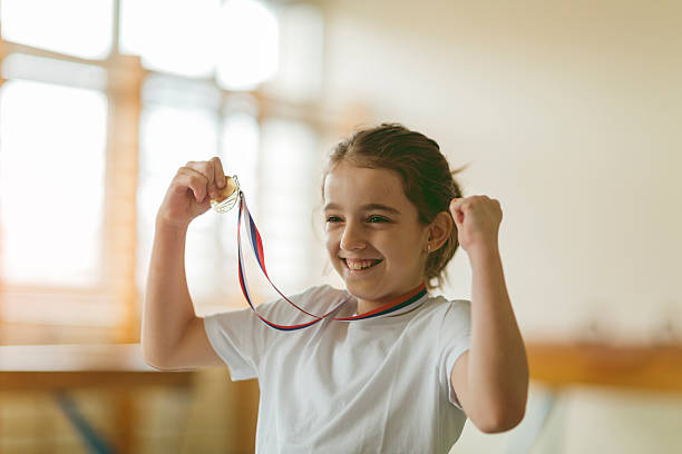 Cute little girl high jumper posing with her gold medal. She is happy and cheerful.