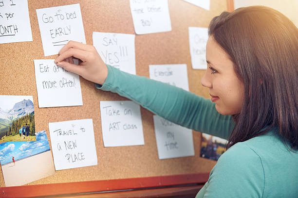Setting her goals Shot of a young woman pinning notes on a corkboard at home adhesive note photos stock pictures, royalty-free photos & images