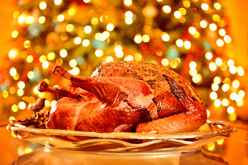 A perfectly browned roasted turkey on a silver platter.  Bokeh from Christmas tree lights in the background.  Some small grain.  Copy space.