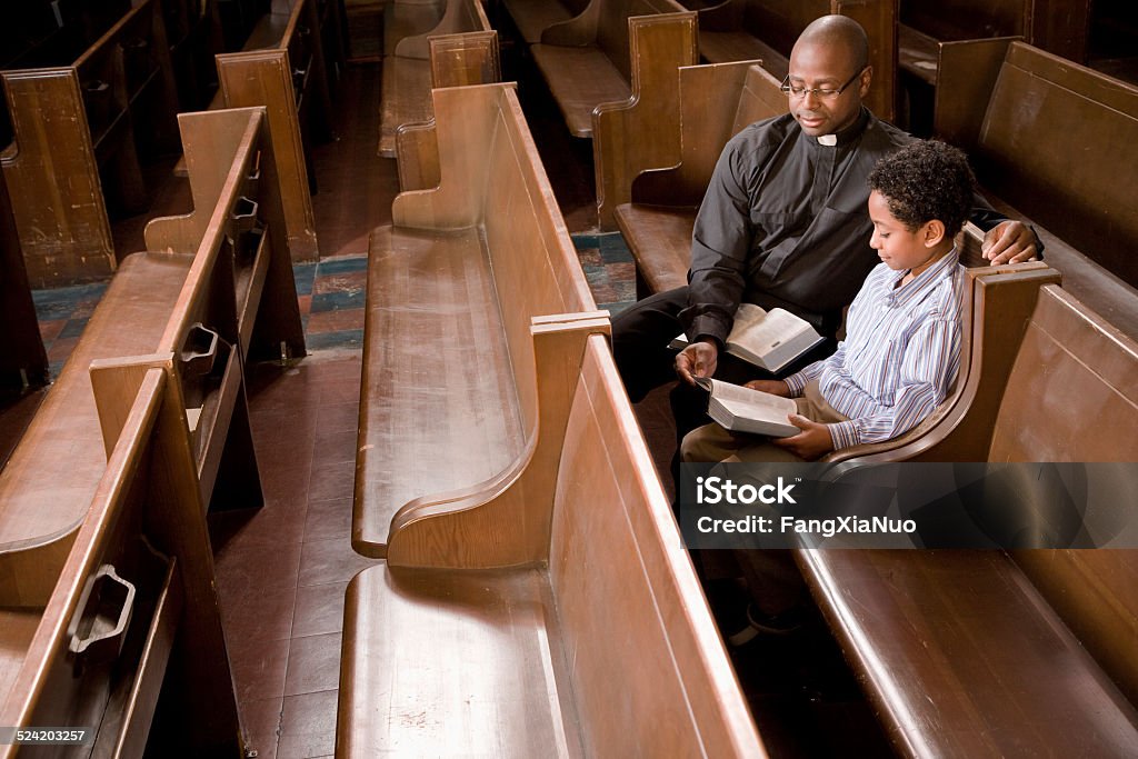 Priest and Boy in Church Pew Reading Bible Priest Stock Photo